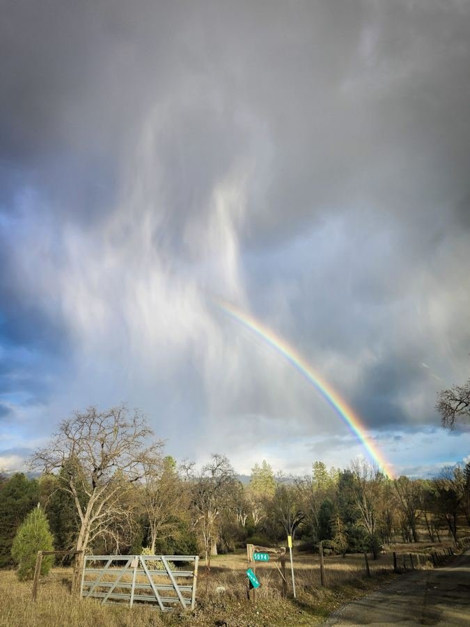 A rainbow arching over a ranch gate under storm clouds in Mariposa