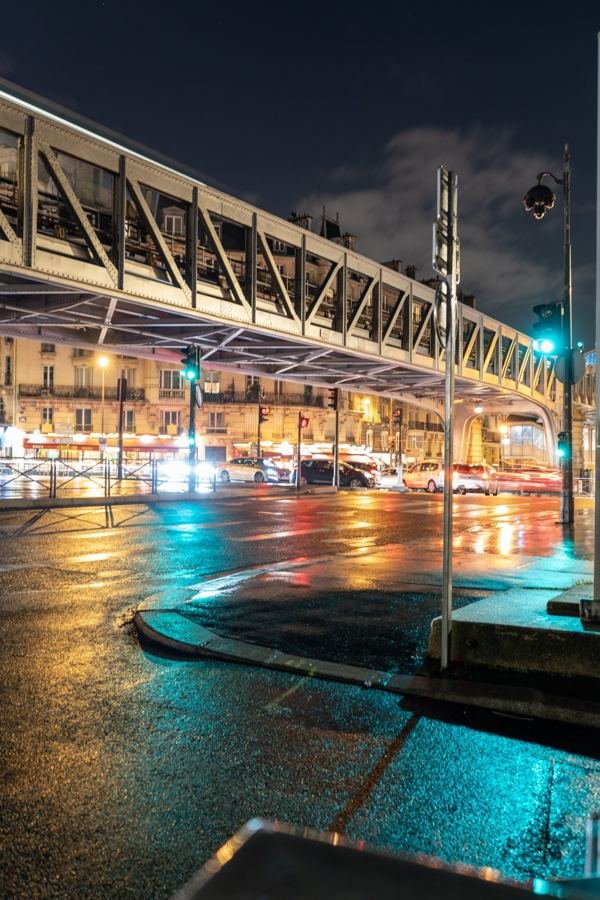 An elevated Paris metro line reflected in wet streets at night